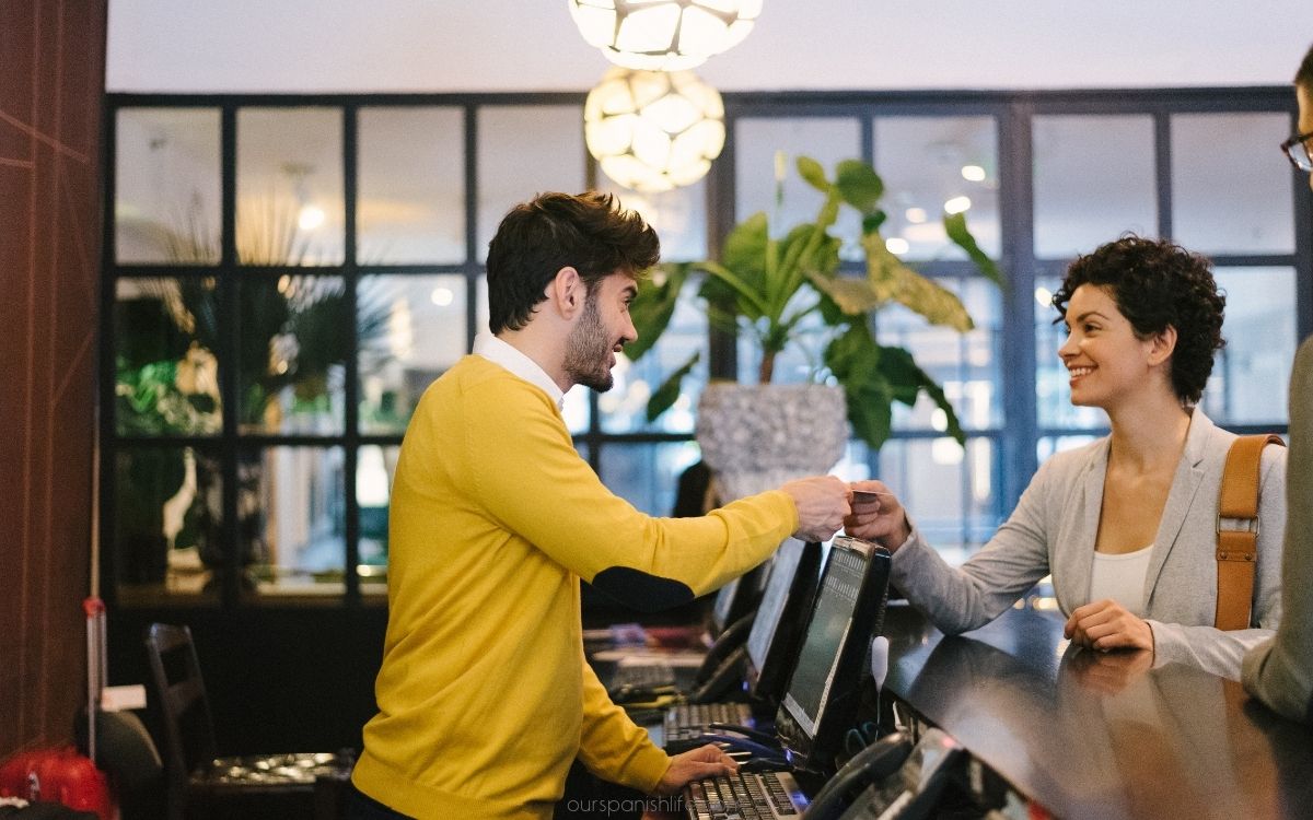 male staff member behind hotel check in desk receiving key from female customer