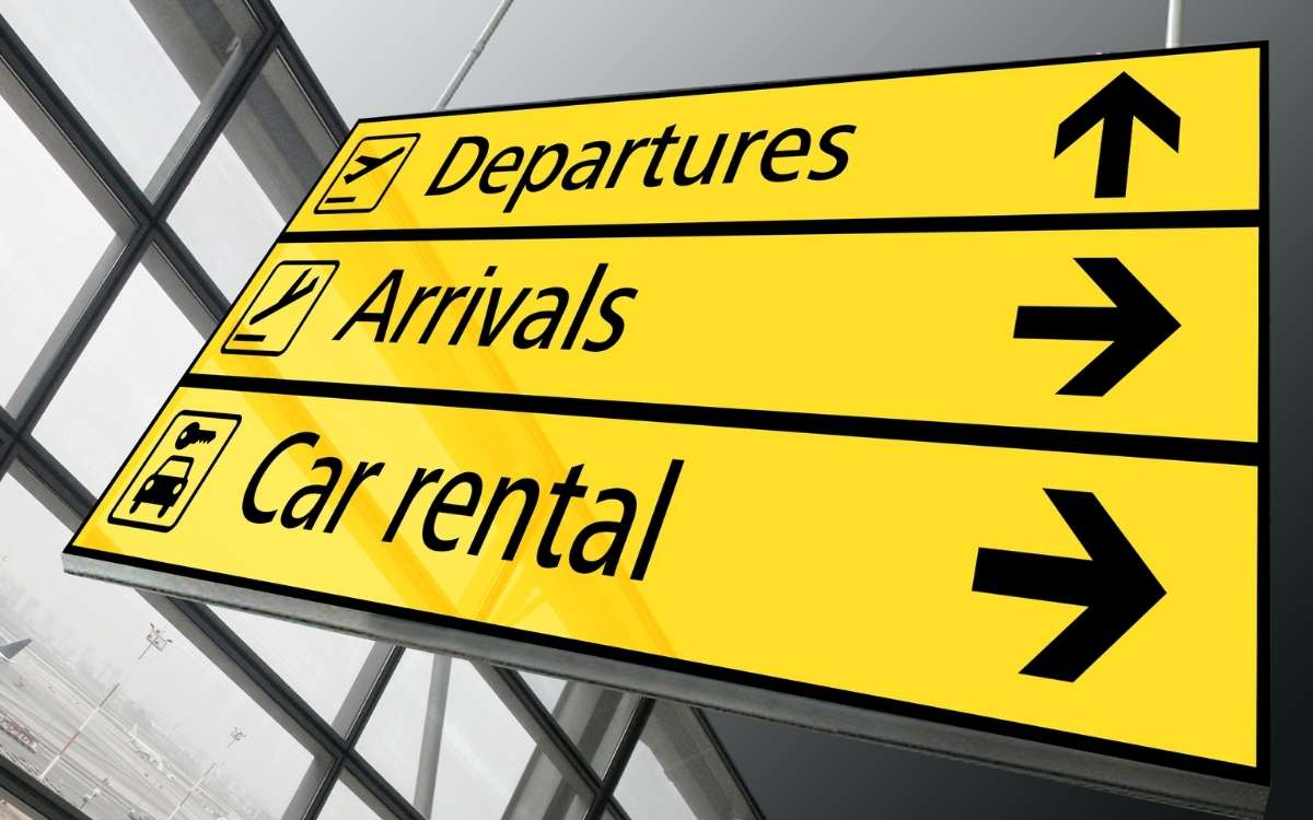 Photo of yellow-colored signs in an airport that reads Departures, Arrivals, and Car Rentals