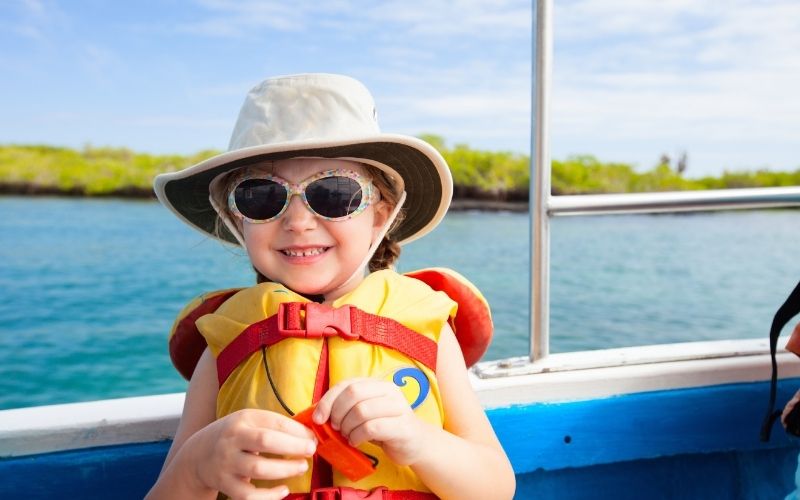 Photo of a child wearing a hat, sunglasses and lifejacket with sea on the background