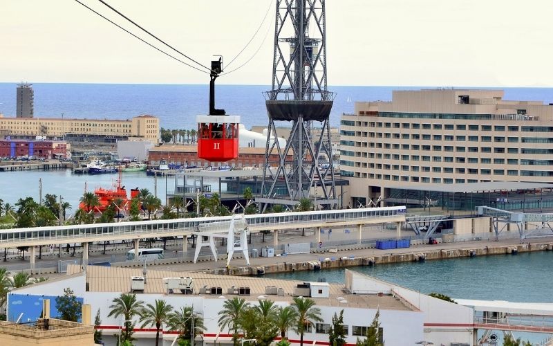 Photo taken from above with buildings, street and seaside below with a red cable car hanging