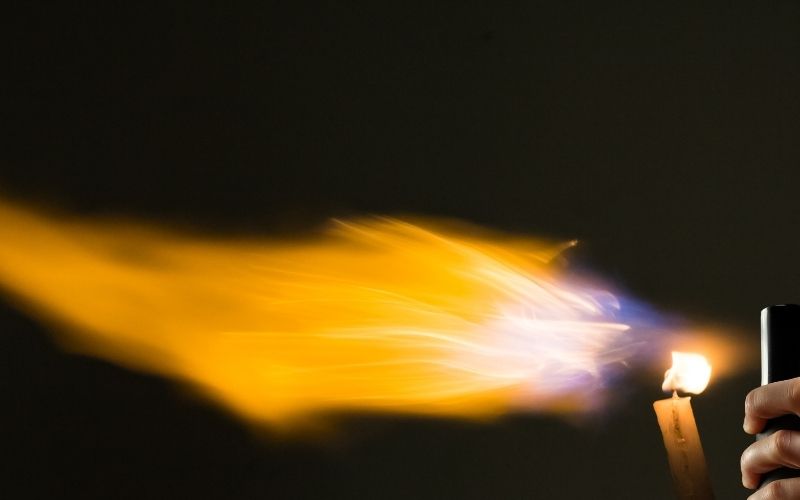 Image of a flame and lit candle with top part of a spray on left side