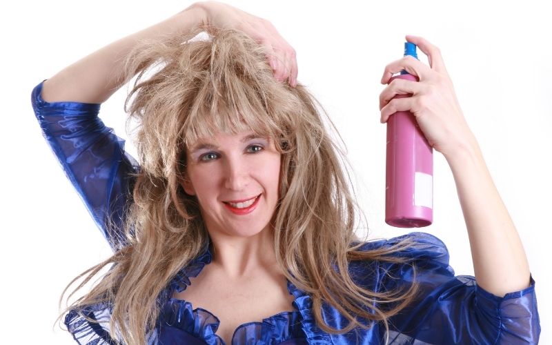 Photo of a woman holding her hair and holding a spray on the other hand pointing to her head