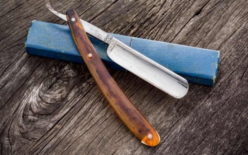 Photo of a straignt razor placed on top of wooden board