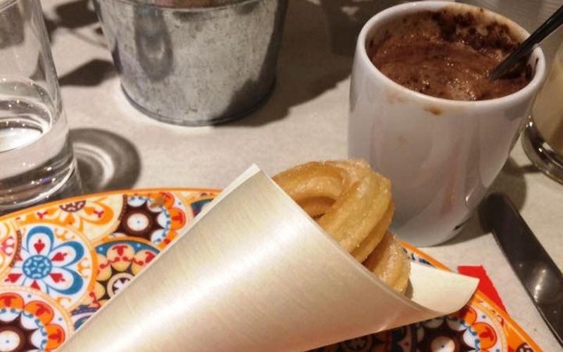Photo of food wrapped in paper and a cup of brown liquid with other utensils on table