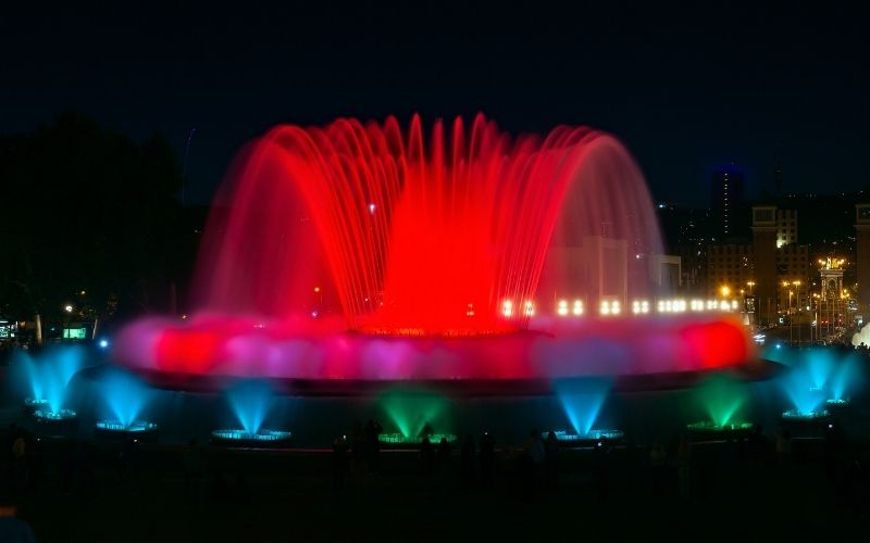 Photo of a park with large fountain sprouting red and blue water