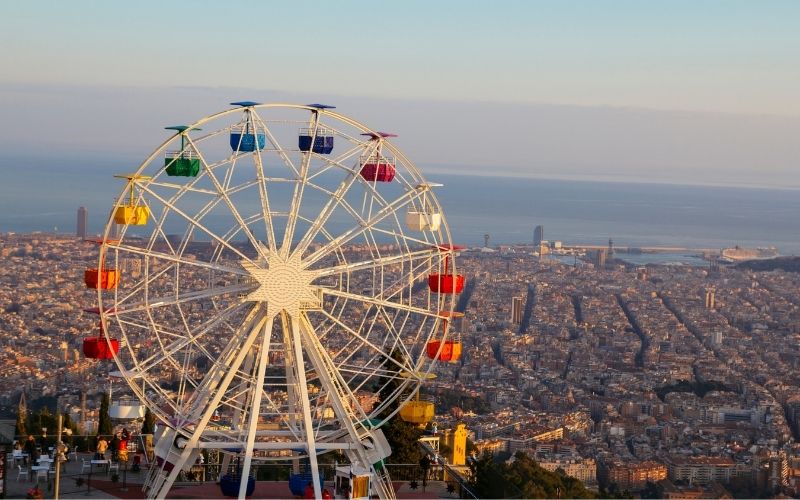 Photo of a ferris wheel in a place with many buildings and streets and sea on background