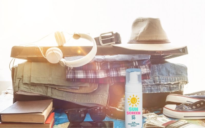Photo showing clothes in a luggage, some books, shades sneakers, and a sunscreen.